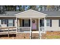 Inviting front porch with a porch swing, white railing, brick foundation, and a pink front door with welcome wreath at 170 Buckaroo Dr, Louisburg, NC 27549