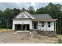 New home featuring brick foundation, covered porch, and an attached garage under construction in a wooded community at 151 Tigris Ct, Zebulon, NC 27597