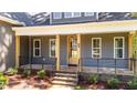 Stone stairs lead to a covered porch featuring a glass front door, windows, and black metal railing at 65 Stream View Way, Spring Hope, NC 27882