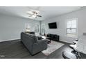 Open living room features modern ceiling fan, grey sofa, dark floors, and outdoor views at 105 Village Dr, Broadway, NC 27505