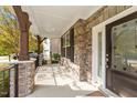 Covered front porch featuring stone columns, wood beams, and a welcoming entrance door at 3409 Lily Orchard Way, Apex, NC 27539