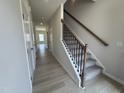 Inviting hallway with wood-look flooring and a carpeted staircase with wrought iron spindles at 76 Commons Cir, Clayton, NC 27520