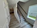Carpeted staircase with dark metal balusters and wood handrail, alongside an open view of the kitchen and a bright window at 84 Commons Cir, Clayton, NC 27520