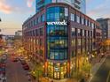 The WeWork building features a brick exterior, large windows, and outdoor seating on a tree-lined street at 110 N Corcoran St # 2302, Durham, NC 27701