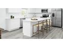 Modern all-white kitchen with gray floors, stainless steel appliances, kitchen island, and seating at 225 N Coral Bells Way, Four Oaks, NC 27524