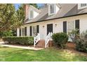Close up of brick steps and a black front door with white siding, black shutters, and manicured landscaping at 7616 Valley Run Dr, Raleigh, NC 27615