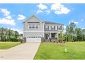 Beautiful home exterior featuring a manicured lawn, stone accents, two-car garage, and classic gray siding under a blue sky at 20 Bold Dr, Youngsville, NC 27596