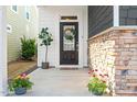 Inviting front porch with stone accents, plants, and a decorative wreath on the black front door at 405 Daisy Grove Ln, Holly Springs, NC 27540