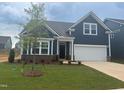 Charming single-Gathering home with manicured lawn, dark blue siding, and a young tree in the front yard at 771 Old Station Pointe, Angier, NC 27501