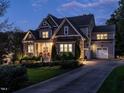 A large 2 story home with a 3-car garage, stone and siding exterior and nicely landscaped front yard illuminated at dusk at 7312 Ridgeline Dr, Raleigh, NC 27613