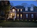 Charming brick home with a welcoming porch, illuminated by landscape lighting in the manicured front yard at dusk at 8508 Kayenta Ct, Wake Forest, NC 27587