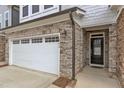 Close up of home front featuring stone accents, one-car garage, black front door, and manicured lawn at 242 Luftee Ln, Holly Springs, NC 27540