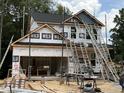 New two-story home under construction with black roof, ladders, open garage, and partially-installed siding at 49 Fetterbush Way, Clayton, NC 27520