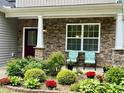 Inviting front porch with stone accents and cheerful chairs surrounded by beautiful plants and flowers at 6021 Watsonia Dr, Zebulon, NC 27597