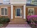 Close-up of the home's entrance boasting a navy door, brick steps, and vibrant pink azaleas in the landscaped front yard at 73214 Burrington, Chapel Hill, NC 27517