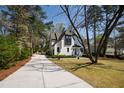 Charming white Tudor-style home featuring a long driveway surrounded by mature trees and lawn at 5004 Lakemont Dr, Raleigh, NC 27609