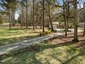 Wide view of the lawn and driveway leading to a charming brick home surrounded by lush trees at 906 Perry Rd, Zebulon, NC 27597