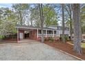 View of exterior with gravel driveway, brick carport, covered porch and mature trees surrounding the home at 927 Ferncrest Dr, Durham, NC 27705
