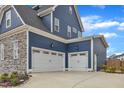 Attached two-car garage with white doors and stone and blue siding on a concrete driveway offers convenience at 1160 Duke Farm Dr, Wake Forest, NC 27587