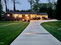 Exterior view of a well-lit home at dusk featuring a long driveway and manicured lawn at 1802 Greenbriar Rd, Henderson, NC 27536