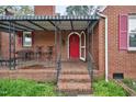Charming brick home featuring a covered front porch, bright red door, and pink shuttered windows at 2724 N Roxboro St, Durham, NC 27704