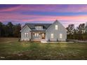 Charming white farmhouse with black trim and stone accents, set against a vibrant twilight sky at 1886 Mays Crossroad Rd, Louisburg, NC 27549