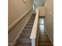 A staircase with carpeted steps, a wood handrail, white trim, and wood-look flooring in a neutral color palette at 9 W Emily Gardens Dr, Selma, NC 27576