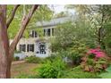 A view of the two-story house through lush trees and greenery, highlighting its yellow siding and black shutters at 1208 College Pl, Raleigh, NC 27605