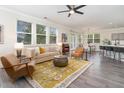 Bright living room featuring hardwood floors, ample seating, large windows, ceiling fan and view into modern kitchen at 112 Mendells Dr, Holly Springs, NC 27540