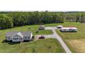 Aerial view of a gray home featuring a detached garage, a play set, and gravel driveway amidst a green field at 8079 Stone Heritage Rd, Middlesex, NC 27557