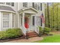 Inviting front porch with a red door, classic white railing, brick steps, and green landscaping at 5405 Whisperwood Dr, Durham, NC 27713