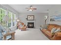 Cozy living room with a fireplace, ceiling fan, large windows, and comfortable leather furniture at 5405 Whisperwood Dr, Durham, NC 27713