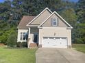 Inviting home featuring a two-car garage, well-manicured lawn, and mature landscaping at 66 Saddle Ln, Lillington, NC 27546