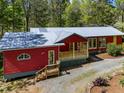 View of the red home with a metal roof and a welcoming wooden porch and stairs at 5401 Friends School Rd, Durham, NC 27705