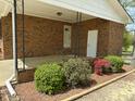 Cozy covered porch featuring brick trim and colorful, mature landscaping and a white door at 1031 Jackson Royster Rd, Henderson, NC 27537