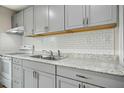 Bright kitchen featuring gray cabinets, granite countertops, stainless steel sink, and white subway tile backsplash at 500 John St St, Clayton, NC 27520