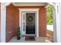 Inviting front entrance with brick surround, a classic black door with a wreath, and manicured greenery at 8721 Owl Roost Pl, Raleigh, NC 27617