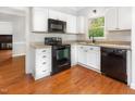 Well-lit kitchen features white cabinets, tile backsplash and black appliances on gleaming hardwood floors at 5013 Dunwoody Trl, Raleigh, NC 27606