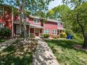 A red townhome with a cozy front porch, surrounded by trees and a green lawn at 116 Old Maple Ln, Durham, NC 27713