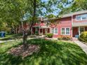 View of a red townhome with a sidewalk, green lawn, and mature trees at 116 Old Maple Ln, Durham, NC 27713
