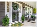 Inviting front porch featuring a decorative wreath, potted plants, rocking chair and a green patterned door mat at 1809 Green Ford Ln, Apex, NC 27502