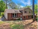 Side view of a two-story home featuring brick and siding with mature trees, set on a sloped lot at 2211 Hillock Dr, Raleigh, NC 27612