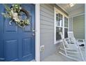 A welcoming front porch with rocking chairs, a wreath on the blue door, and a window at 6511 Academic Ave, Raleigh, NC 27616