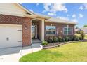 A view of the red brick exterior with a well-manicured flower garden surrounding the front door at 8 Pal Ct, Benson, NC 27504