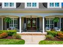 Inviting front porch with white columns, black shutters, seating, and decorative wreaths on the double front doors at 658 Bennett Mountain Trce, Chapel Hill, NC 27516