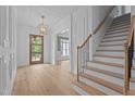 Bright foyer with hardwood floors, statement lighting, white wainscoting and millwork, and a clear view of the staircase at 7301 Wexford Woods Ln, Wake Forest, NC 27587