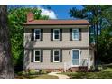 Charming two-story home featuring a blue front door, neutral siding, and black shutters, set amidst mature trees and green lawn at 3317 E Jameson Rd, Raleigh, NC 27604