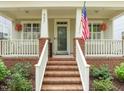 Inviting brick front porch with white railings, hanging floral baskets, and an American flag on display at 607 Millbrook Dr, Pittsboro, NC 27312