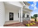 Inviting front porch featuring brick steps, black railing, black front door, and stylish architectural details at 203 Sourgum Ct, Zebulon, NC 27597