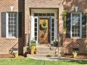 Close-up of front entry door with wreath, sidelights, planters, and brick facade at 308 Sunset Creek Cir, Chapel Hill, NC 27516